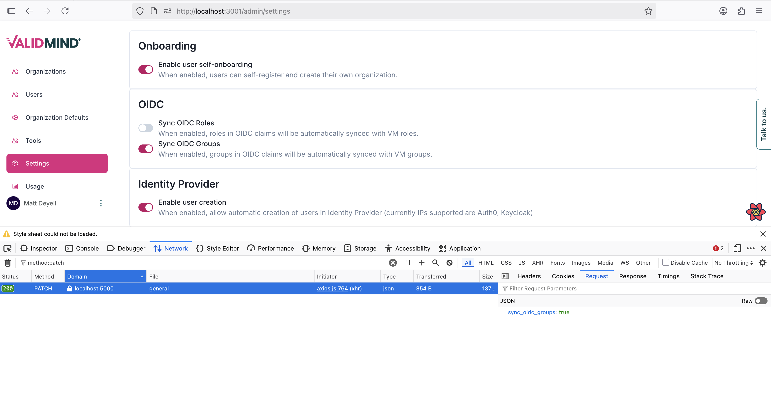A web interface displaying an admin settings page for an application. The left sidebar features a navigation menu with sections for Organizations, Users, Organization Defaults, and Settings, highlighted in pink. The main content area includes three sections: Onboarding, OIDC, and Identity Provider, each with toggle switches and descriptions, such as enabling user self-onboarding and syncing OIDC roles and groups. The top navigation bar shows the URL localhost:3000/admin/settings, and the bottom section displays a browser developer tools panel with tabs like Elements, Console, and Network, with the Network tab active showing a request to the endpoint /api/v1/oidc_sync_groups. The page has a clean layout with a white background and pink accents.